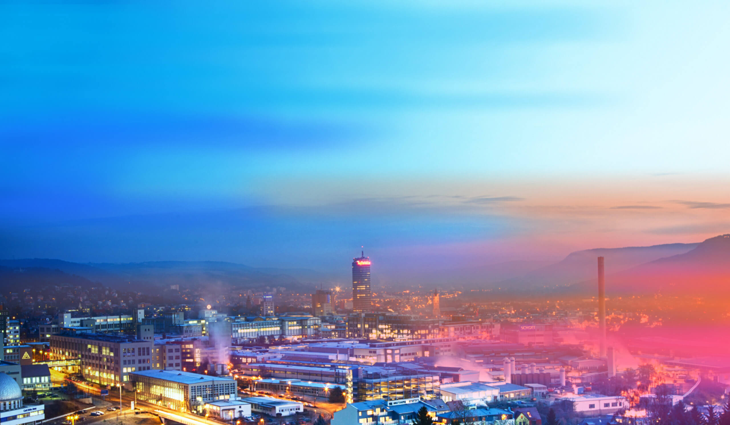 Stadtansicht von Jena bei Dämmerung mit beleuchteten Gebäuden und dem Jentower im Zentrum. Ein farbiger Verlauf in Blau und Pink liegt über dem Bild