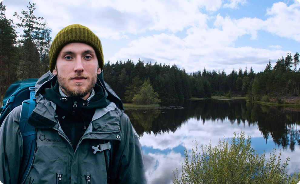 Porträt eines Mannes in Outdoor-Kleidung. Im Hintergrund ist eine See- und Waldlandschaft