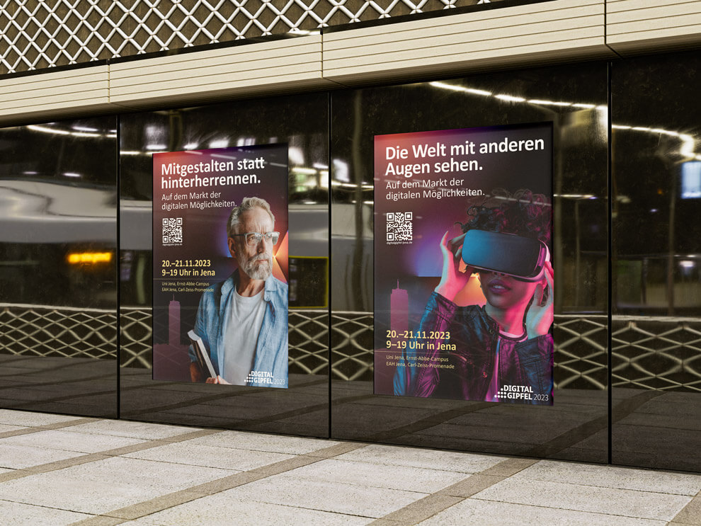 Zwei große Plakate an einer Glaswand in einer U-Bahn- oder Bahnhofsumgebung werben für ein Event zu digitalen Möglichkeiten in Jena. Sie zeigen unterschiedliche Personen, Headlines, QR-Codes sowie Datum und Veranstaltungsinformationen