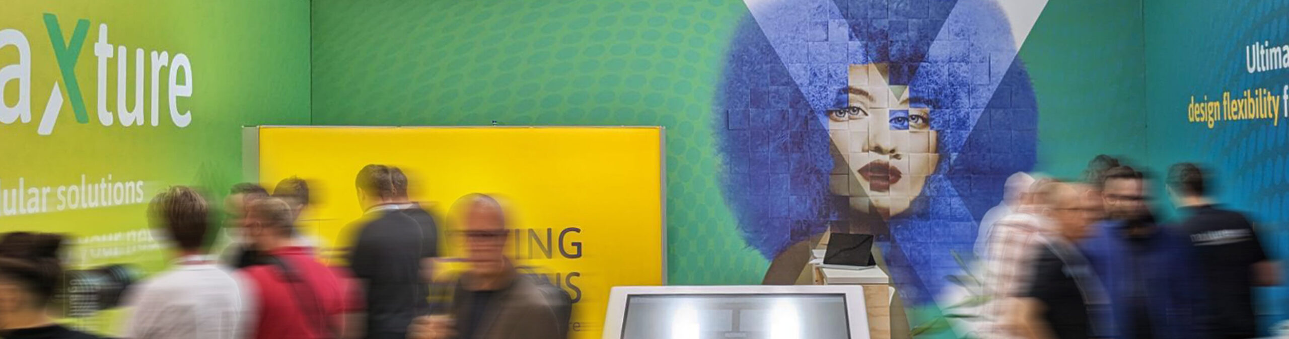 Besucher bewegen sich vor einem Messestand mit großformatiger Wandgrafik und Präsentationsfläche
