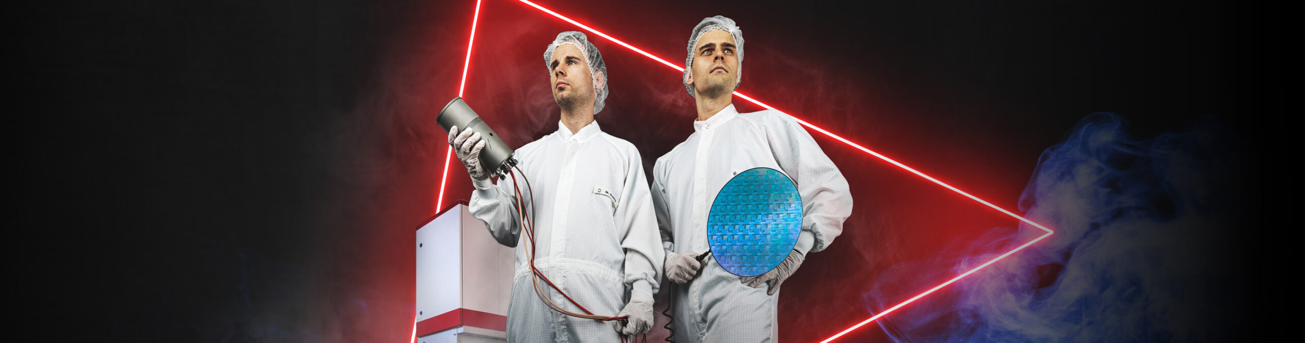 Zwei Fachkräfte in weißen Reinraumanzügen stehen selbstbewusst vor einer technischen Anlage und halten ein Bauteil sowie eine runde Siliziumscheibe in der Hand, während im Hintergrund rote Neonlinien und Nebel eine futuristische Laboratmosphäre erzeugen