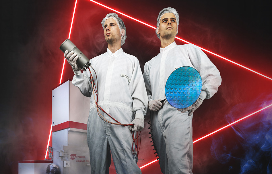 Zwei Fachkräfte in weißen Reinraumanzügen stehen selbstbewusst vor einer technischen Anlage und halten ein Bauteil sowie eine runde Siliziumscheibe in der Hand, während im Hintergrund rote Neonlinien und Nebel eine futuristische Laboratmosphäre erzeugen