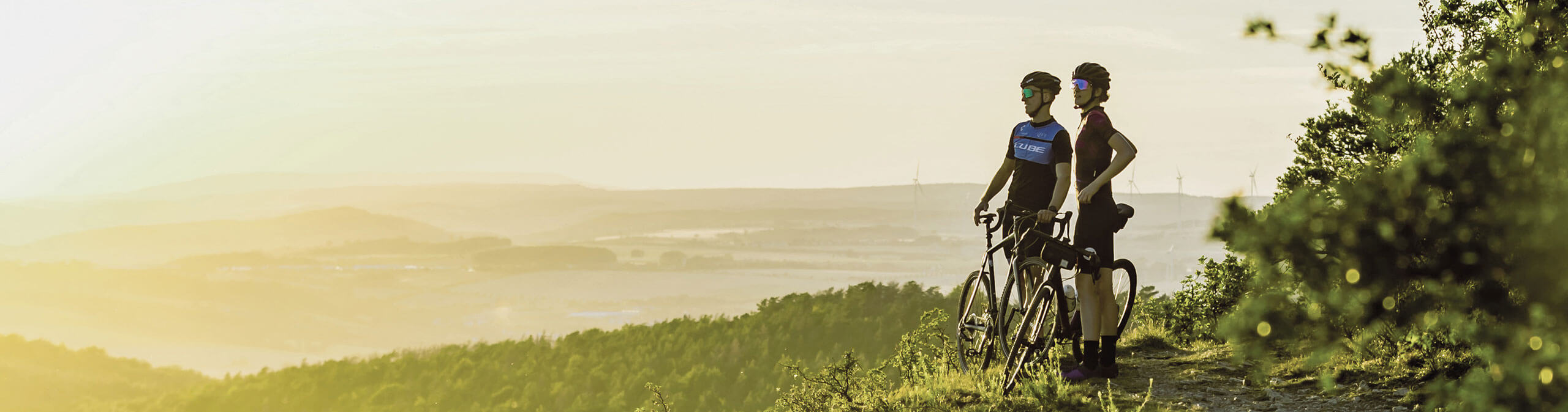 Radfahrer mit Rennrädern auf Aussichtspunkt in Thüringens Süden mit Blick über Landschaft und Windräder bei Sonnenuntergang
