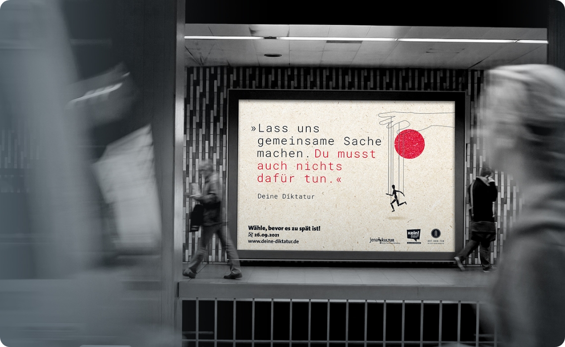 Großes Kampagnenplakat „Deine Diktatur“ an einer U-Bahn-Wand, während Passanten vorbeigehen
