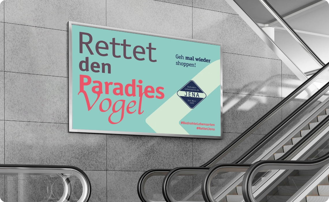 Großes Werbeplakat mit dem Motiv „Rettet den Paradiesvogel“ an einer Wand neben Rolltreppen in einer modernen Einkaufspassage