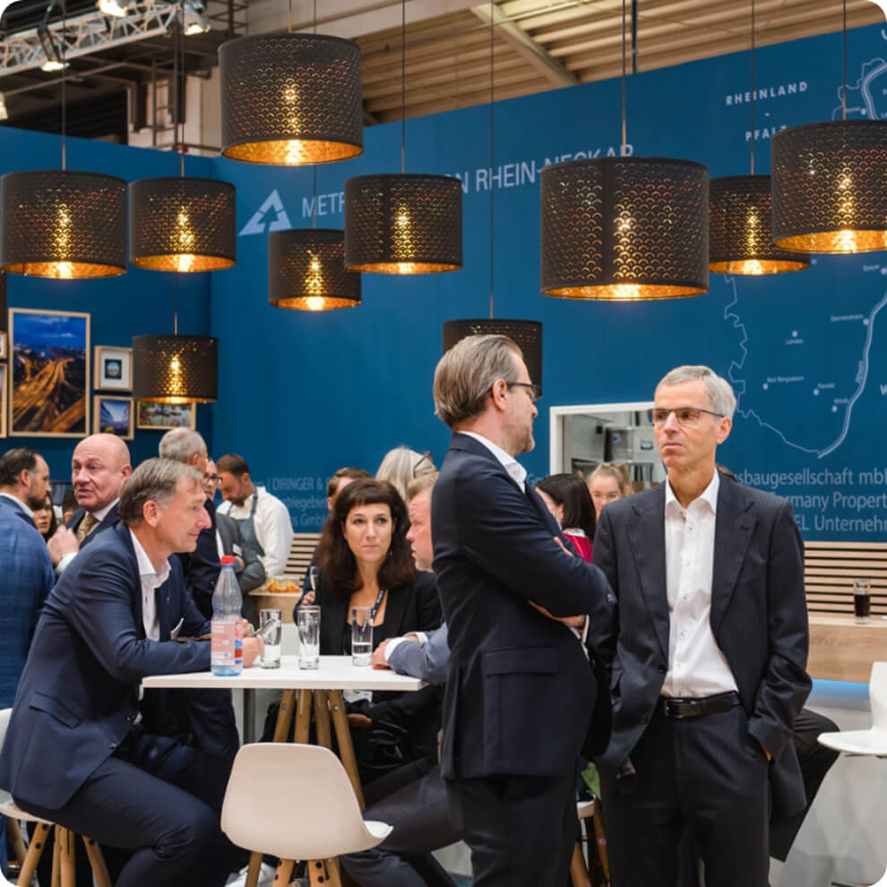 Besucherinnen und Besucher führen Gespräche an Stehtischen auf dem Messestand der Metropolregion Rhein-Neckar