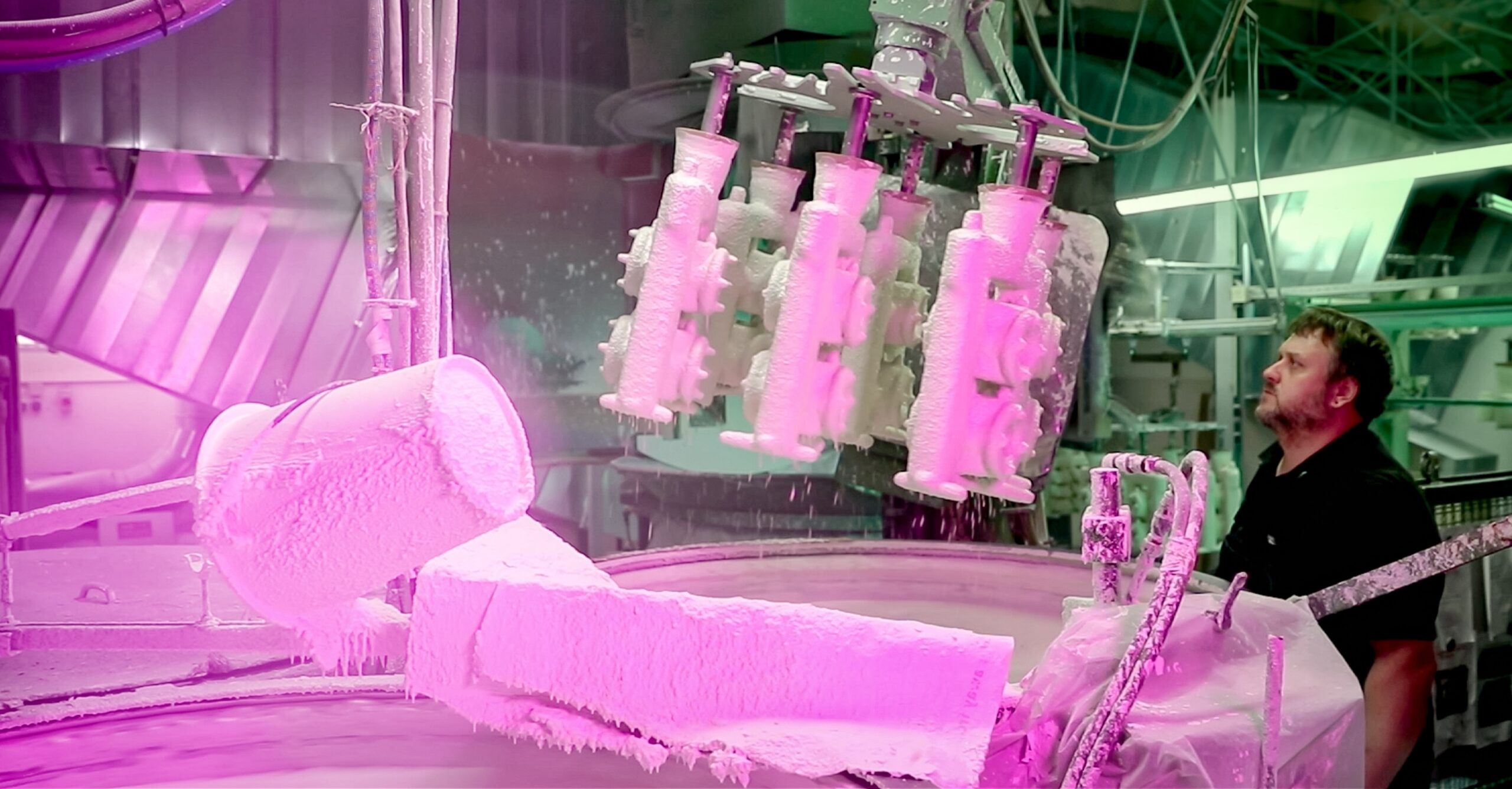 Ein Mitarbeiter überwacht in der Produktion einen keramischen Beschichtungsprozess im Feinguss, bei dem mehrere Bauteile automatisiert in ein Tauchbecken eingetaucht und für den späteren Metallguss vorbereitet werden