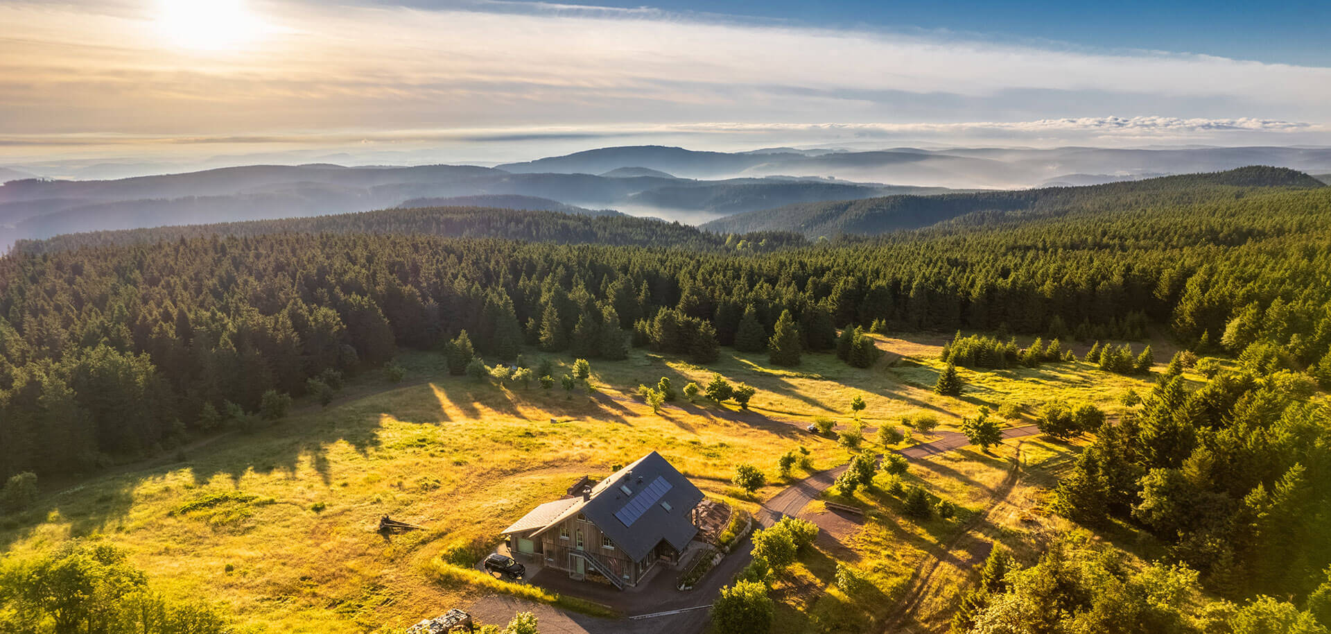 Landschaftspanorama in Thüringens Süden mit Haus am Waldrand und weiter Aussicht über Wälder und Hügel bei Sonnenaufgang