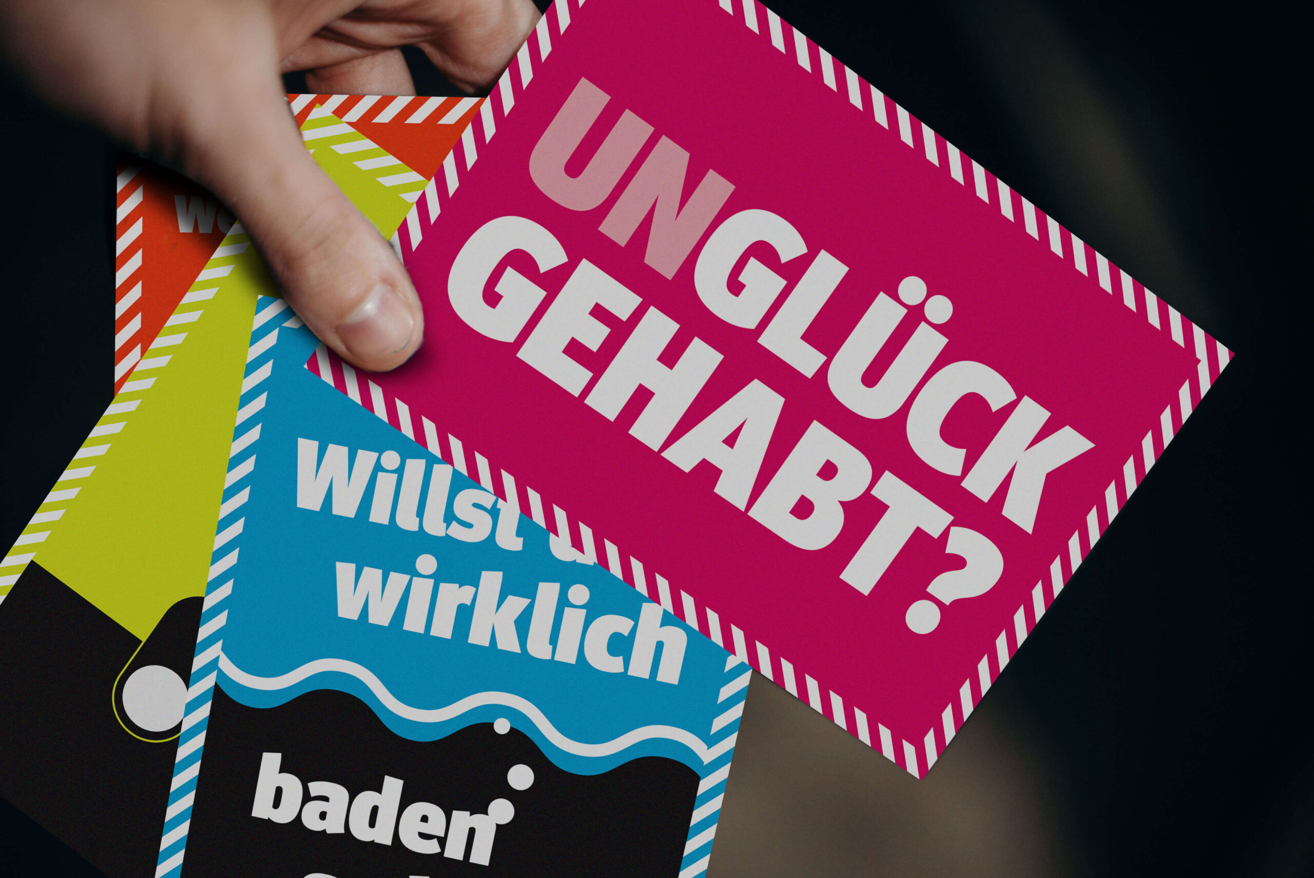 Hand hält mehrere farbige Postkarten einer Informationskampagne zum Bevölkerungsschutz, darunter eine Karte mit der Frage „Unglück gehabt?“ und Hinweisen zu richtigem Verhalten in Gefahrensituationen