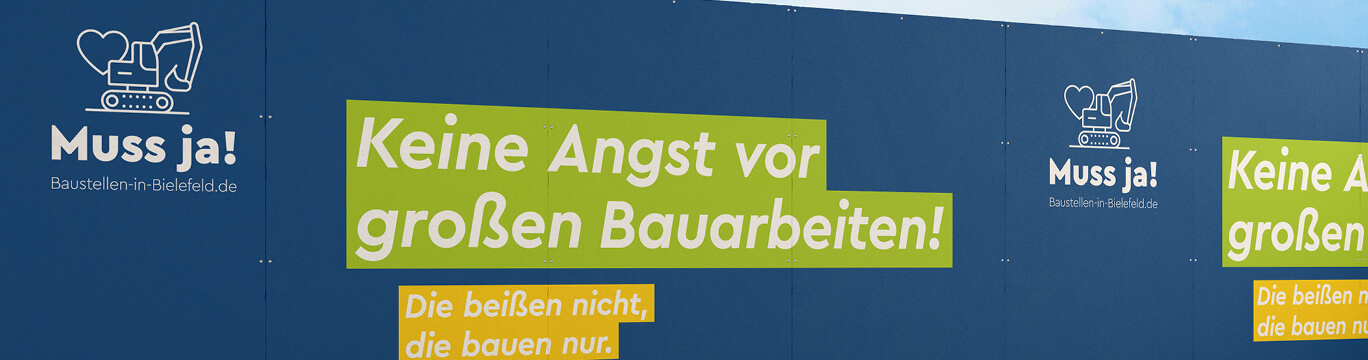 Blauer Bauzaun mit Kampagnenmotiv „Muss ja!“ und der Botschaft „Keine Angst vor großen Bauarbeiten! Die beißen nicht, die bauen nur.“ zur Information und Beruhigung von Bürgerinnen und Bürgern an einer Baustelle