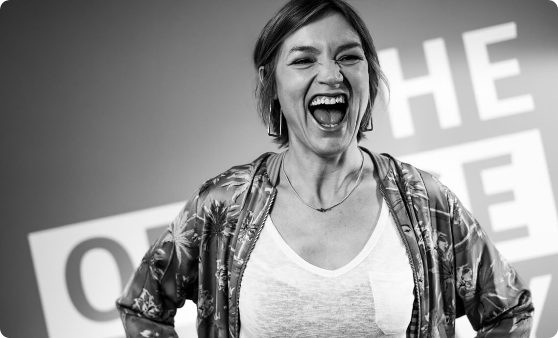 Porträt einer lachenden Mitarbeiterin vor Unternehmensbranding als Bildmotiv für Teamkultur und positive Arbeitsatmosphäre