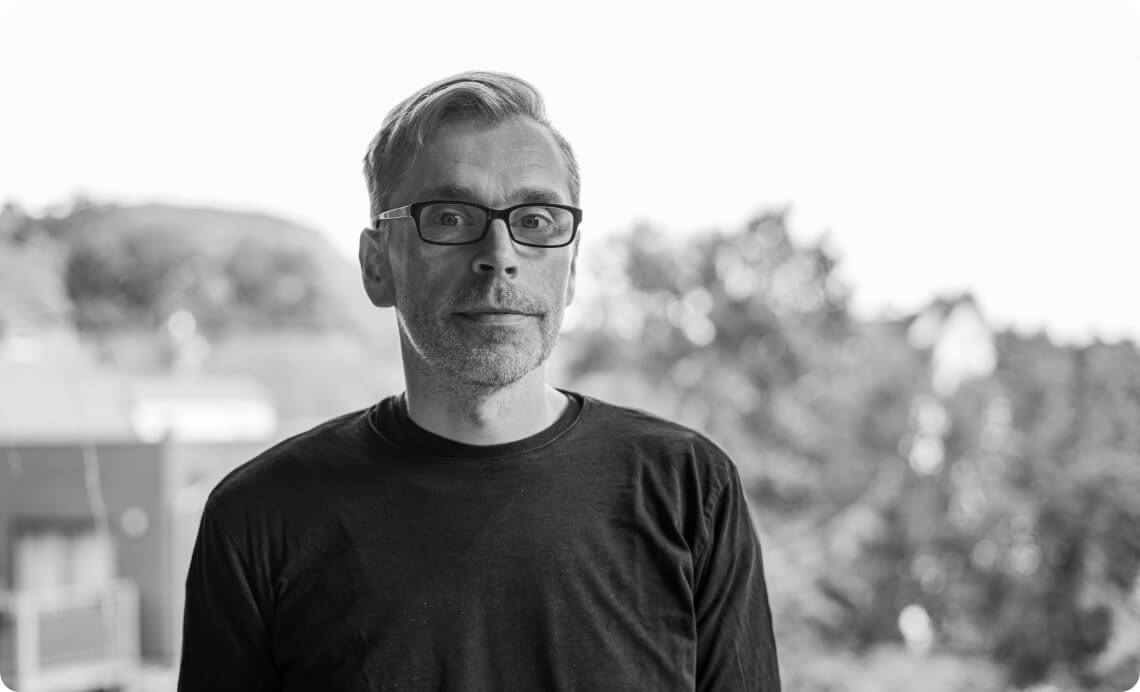 Porträt eines Mitarbeiters mit Brille vor unscharfem Außenhintergrund, als ruhiges Bildmotiv für Kompetenz, Verlässlichkeit und persönliche Präsenz