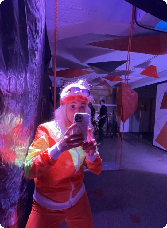 32 Person in auffälligem Kostüm fotografiert mit Smartphone bei Indoor-Event als Bildmotiv für Teamevent und kreative Unternehmenskultur