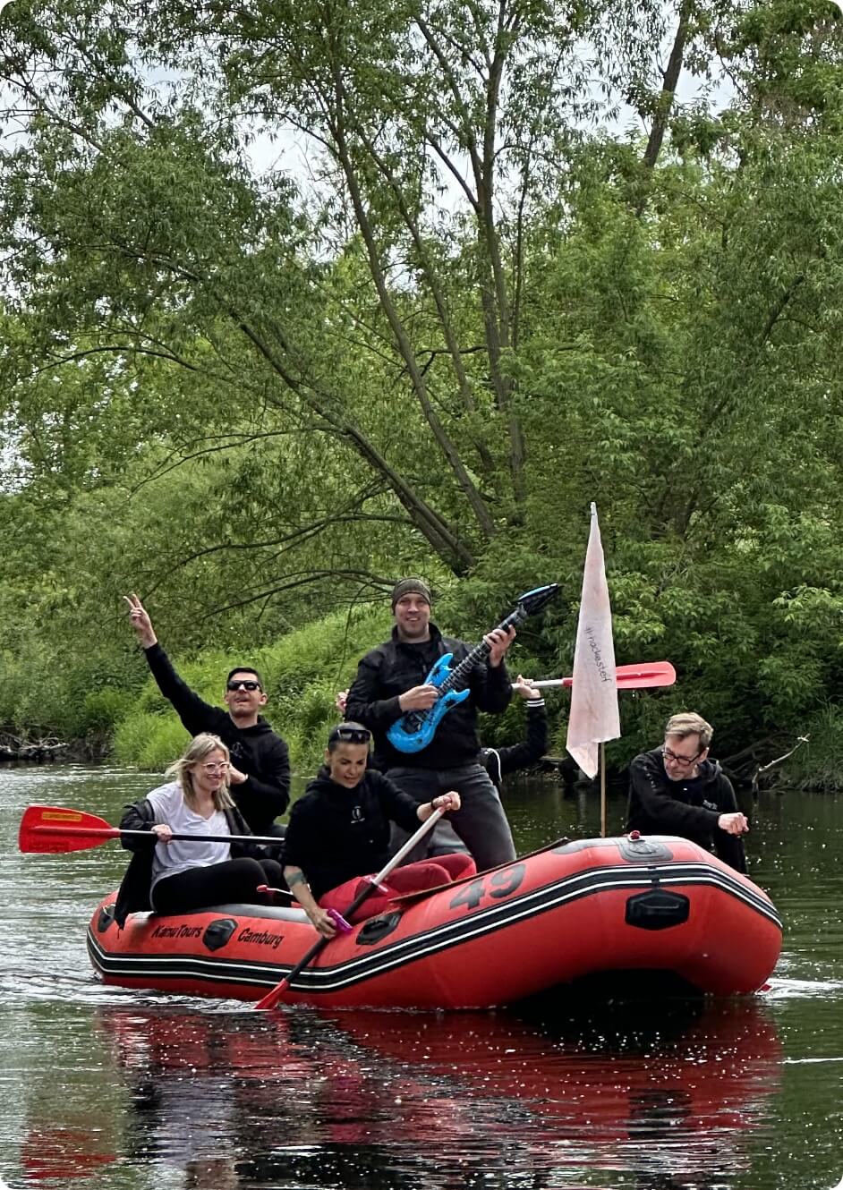 Teamgruppe bei Kanutour auf Fluss mit humorvoller Aktion als Bildmotiv für Teambuilding und Betriebsausflug