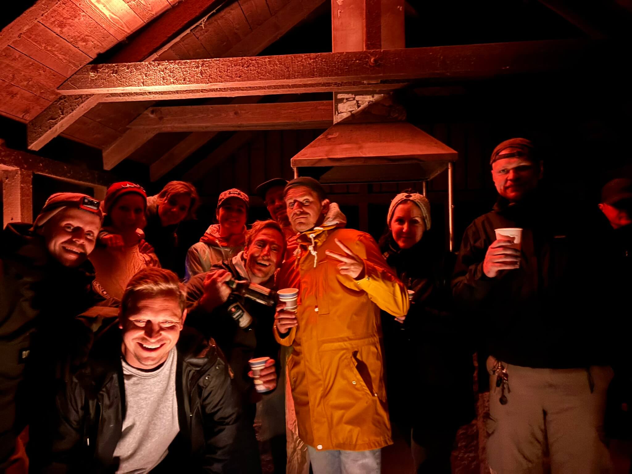 Teamtag_Team Gruppe von Mitarbeitenden steht abends in einer Hütte zusammen, hält Becher in der Hand und lacht in die Kamera, als Bildmotiv für Gemeinschaft, Zusammenhalt und Teamkultur
